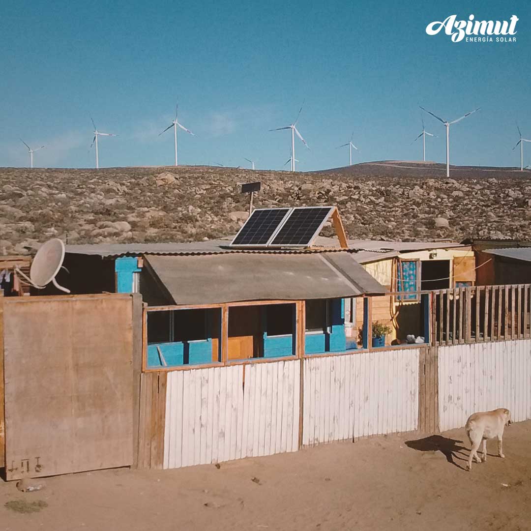 Paneles solares sobre una casa costera con aerogeneradores al fondo